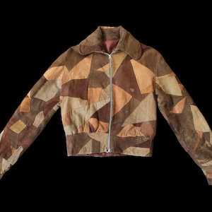 May include: A brown patchwork jacket with a zip fastening. The jacket features a variety of geometric shapes in shades of brown, tan, and beige. The jacket has a collar and long sleeves. The jacket is displayed against a black background.