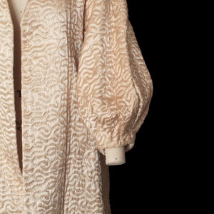 May include: A long, cream-colored quilted robe with a shawl collar and long sleeves. The robe has a unique, swirling pattern.