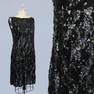 May include: A sleeveless black sequined dress with a scoop neckline. The dress is made of a shimmering fabric with a subtle pattern.