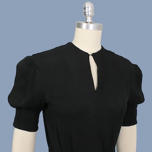 May include: A black short-sleeved dress with a keyhole neckline and puff sleeves.