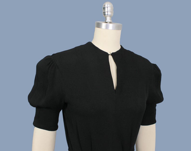 May include: A black short-sleeved dress with a keyhole neckline and puff sleeves.