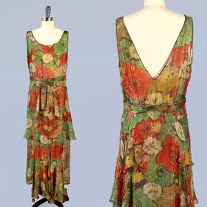 Könnte beinhalten: Ein ärmelloses Maxikleid mit einem Blumendruck in Rot-, Grün- und Goldtönen. Das Kleid hat einen V-Ausschnitt und ein tailliertes Oberteil. Der Rock ist gestuft und hat einen Rüschen-Saum.