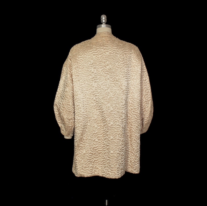May include: A cream-colored quilted jacket with a textured pattern. The jacket has long sleeves and a collar.