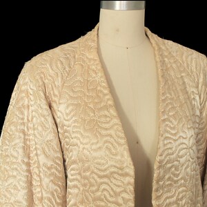 May include: A cream-colored quilted jacket with a V-neck and a swirling pattern.