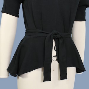 May include: A black, short-sleeved top with a fitted bodice and a flowing, asymmetrical peplum hem. The top features a self-tie belt at the waist.