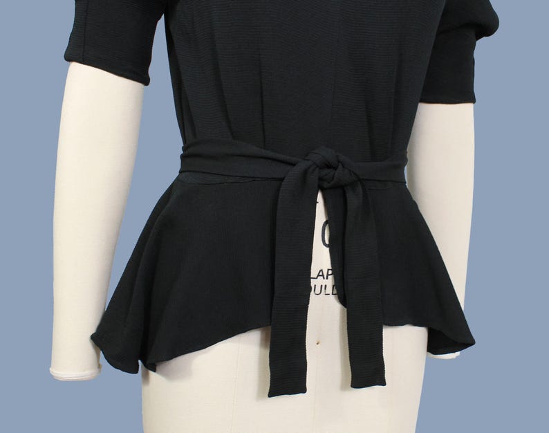 May include: A black, short-sleeved top with a fitted bodice and a flowing, asymmetrical peplum hem. The top features a self-tie belt at the waist.
