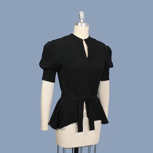 May include: A black, short-sleeved blouse with a keyhole neckline and a fitted waist. The blouse has a peplum hem and a self-tie belt.