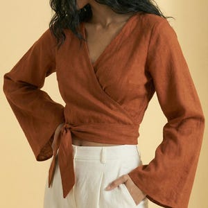 Puede incluir: Top envolvente de color óxido con mangas largas y acampanadas y cierre de lazo. Combinado con pantalones blancos. El top tiene un escote en V y está hecho de una tela texturizada. Los pantalones tienen pernera recta y un bolsillo.