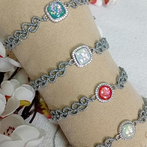 May include: Four silver bracelets with iridescent gemstone centres. The bracelets feature a delicate, openwork design. The gemstones are square and round, in shades of green, white, and red. A close-up view.