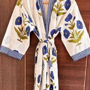 May include: White cotton robe with a blue floral pattern and blue striped trim. The robe features a tie closure and wide sleeves. The floral design includes blue flowers and green leaves. The robe is hanging on a wooden hanger.