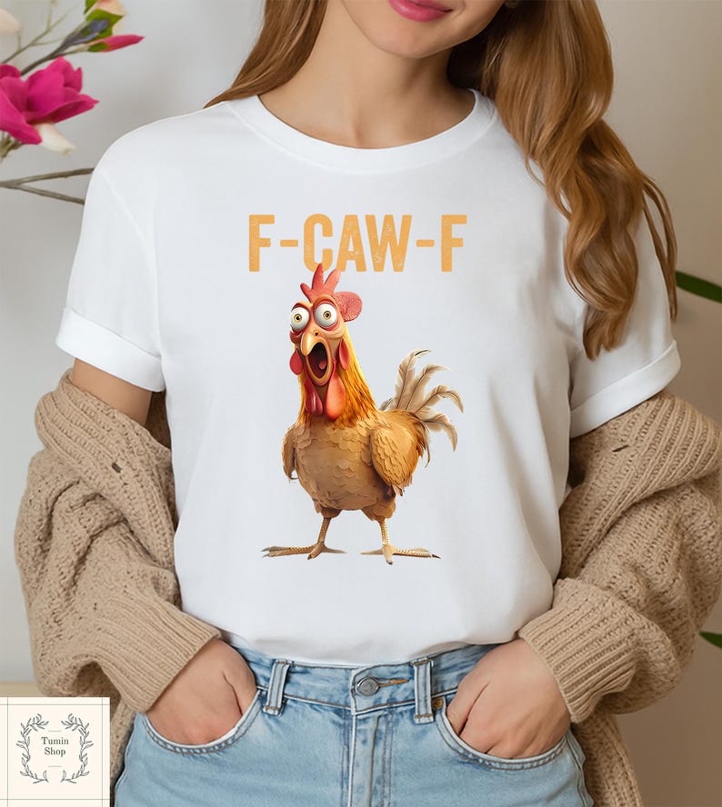 May include: White t-shirt featuring a cartoon chicken with an open beak and the text "F-CAW-F" in orange. The chicken is brown, orange, and red with wide eyes. The shirt has rolled-up sleeves.