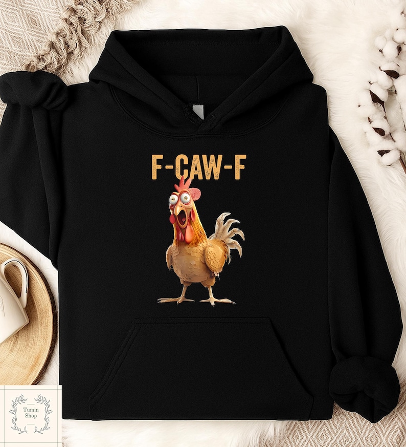 May include: Black hooded sweatshirt featuring a cartoon chicken with wide eyes and an open beak. The text "F-CAW-F" is printed above the chicken. The chicken is brown, red, and yellow.