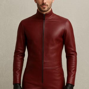 May include: A burgundy leather jumpsuit with a high collar and a full-length black zipper. The long-sleeved garment includes a waist seam and pockets. The person is wearing black leather gloves.