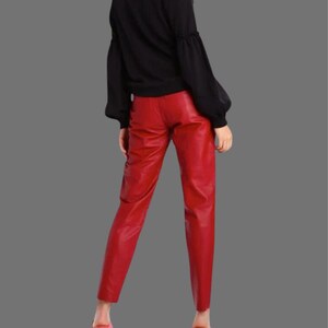 May include: Red leather pants with a straight leg cut. The pants are a vibrant red color and appear to be made of a smooth leather material. The pants are paired with a black top.