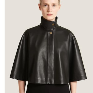 May include: A black leather cape with a high collar and two gold-colored buttons. The cape has a smooth texture and a classic design, suitable for outerwear.