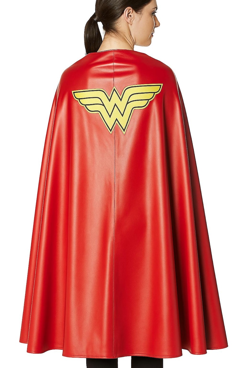 May include: A red cape with a yellow and black emblem on the back. The cape is made of a shiny material and is designed to be worn. The emblem is a stylized "W" with wings, a superhero-themed costume accessory.