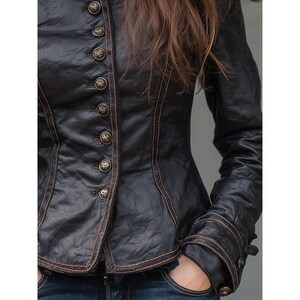 May include: Black leather jacket with ornate brass buttons and decorative stitching. The jacket features a fitted silhouette, long sleeves, and a high collar. The jacket's design is reminiscent of vintage or steampunk styles.