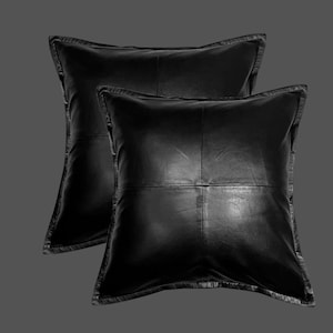 May include: Two square black leather cushions. Each cushion features a stitched square pattern in the centre and a stitched border. The cushions are displayed on a grey background.