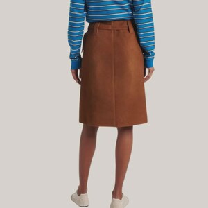 May include: A brown suede skirt with a belt and a knee-length hemline. The skirt is paired with a blue and white striped long-sleeve shirt and white sneakers. The skirt is a classic, versatile piece.