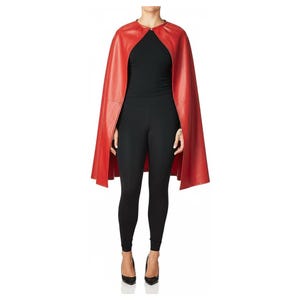 May include: A vibrant red leather cape with a round neckline and a front closure. The cape is worn over a black top and black leggings. The model is wearing black high heels.