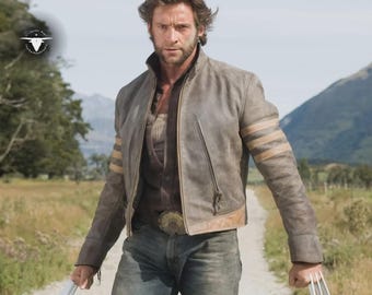 May include: A grey leather jacket with tan stripes on the sleeves and a zip closure. The jacket is worn over a brown shirt and blue jeans. The person is holding metal claws. The background features a dirt path and mountains.