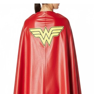 May include: A red cape with a yellow emblem featuring a stylized "W" with wings. The cape is made of a smooth material and drapes down the back. The emblem is centered on the upper back of the cape.