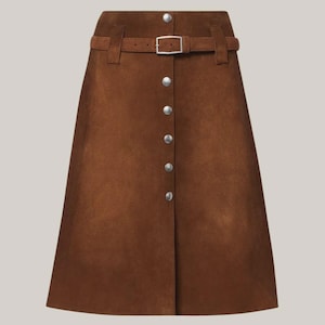 May include: A brown suede skirt with a button-down front and a matching belt. The skirt has a classic A-line shape and features silver-colored buttons and a buckle. The belt is secured with a silver-colored buckle.