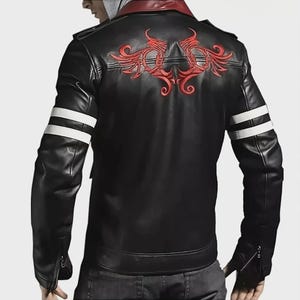 May include: A black jacket featuring a red embroidered design on the upper back, a dark red collar, and two horizontal white stripes on each sleeve. The jacket has long sleeves with zippered cuffs and is worn over a grey hooded garment.
