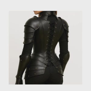 May include: Black leather armour featuring shoulder pauldrons, arm guards, and a corset-style back. The armour is detailed with rivets and a lace-up closure. The garment is worn over a black long-sleeved top.