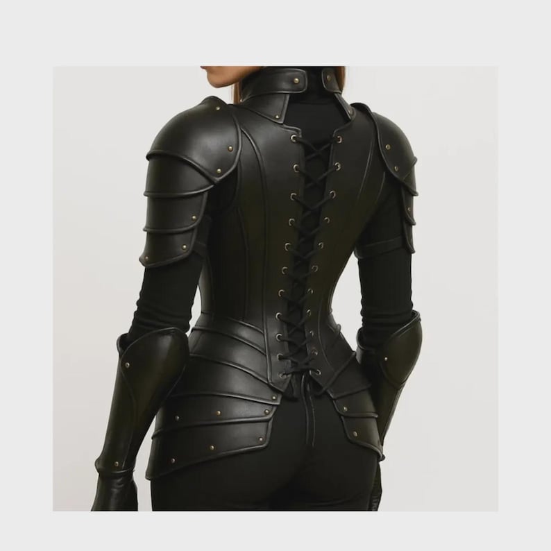 May include: Black leather armour featuring shoulder pauldrons, arm guards, and a corset-style back. The armour is detailed with rivets and a lace-up closure. The garment is worn over a black long-sleeved top.