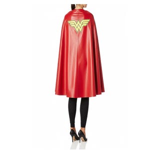 May include: A red cape with a yellow emblem on the back. The cape is made of a shiny material and is knee-length. The emblem is a stylized "W" with wings. The person is wearing black leggings and black high heels.
