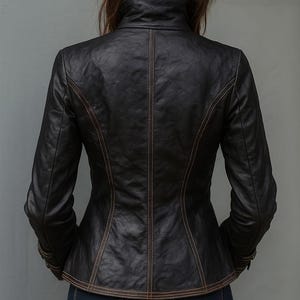 May include: A black leather jacket with a high collar and long sleeves. The jacket features decorative stitching in a contrasting brown color along the seams and edges. The back of the jacket is visible, showcasing its tailored fit.