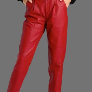 May include: A pair of bright red leather pants. The pants have a high waist and a tailored fit, with pleats at the front. The leather appears smooth and has a slight sheen, reflecting the light. The pants are a solid, vibrant color.