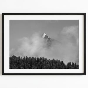 Peut inclure: Tirage encadré en noir et blanc d'un sommet montagneux émergeant des nuages. La montagne est partiellement cachée par le brouillard, avec une forêt de conifères au premier plan. L'impression est dans un cadre noir.