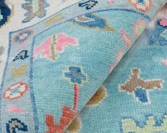 Könnte beinhalten: Nahaufnahme eines Teils eines türkisfarbenen und cremefarbenen Teppichs mit detailliertem Blumenmuster. Der Teppich hat einen Rand mit geometrischen Formen und ein zentrales Design mit rosa, blauen und orangefarbenen floralen Elementen. Der Teppich ist gefaltet und zeigt seine Textur.
