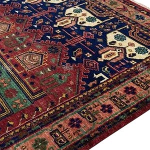 Puede incluir: Una alfombra con un detallado diseño geométrico. La alfombra presenta un campo central azul marino intenso con detalles en rojo, verde y crema. El borde es una mezcla de motivos rojos, marrones y florales, creando una estética tradicional.