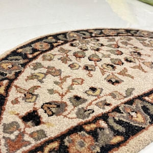 May include: A semi-circular rug with a beige central field featuring a floral pattern in shades of brown, green, and yellow. The border is a dark color with floral motifs. The rug is made of a soft, textured material.
