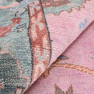 Pode incluir: Close-up de um tapete enrolado com um padrão detalhado. O tapete apresenta uma combinação de cores, incluindo rosa, verde-azulado e vermelho. O design incorpora formas geométricas e motivos florais, criando uma aparência texturizada.