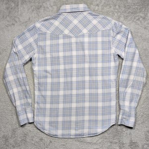May include: A long-sleeved button-down shirt with a plaid pattern in white and light blue. The shirt has a classic collar and buttoned cuffs. The back of the shirt is visible, showing the yoke detail.