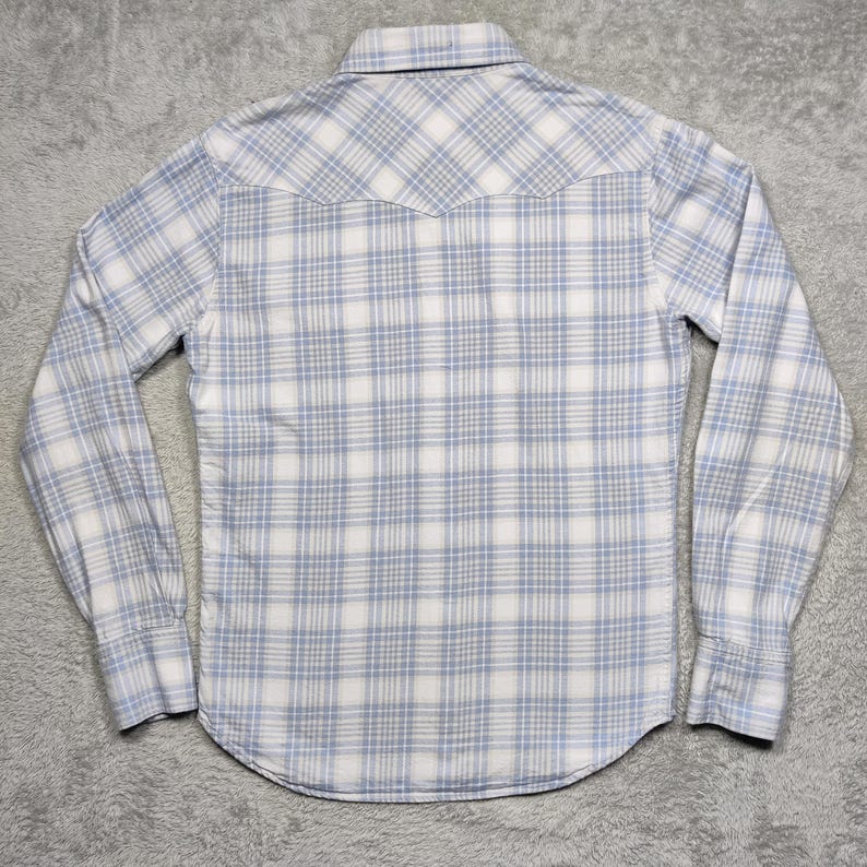 May include: A long-sleeved button-down shirt with a plaid pattern in white and light blue. The shirt has a classic collar and buttoned cuffs. The back of the shirt is visible, showing the yoke detail.