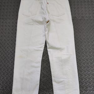 May include: White denim trousers with a classic five-pocket design. The trousers feature a red Levi's tag on the back pocket and a brown leather patch at the waistband. The trousers are clean and show minimal wear.