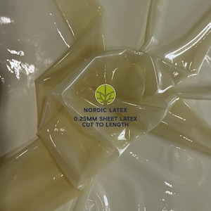 May include: A translucent, pale yellow sheet of latex with a glossy finish. The material is folded and draped, showing its flexible texture. Printed text on the surface reads NORDIC LATEX 0.25MM SHEET LATEX CUT TO LENGTH with a green tree logo.