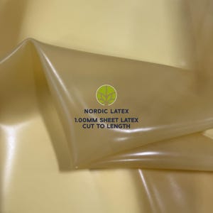Puede incluir: Una lámina de látex translúcida de color amarillo pálido con una textura suave y flexible. La superficie presenta un logotipo circular verde con un icono de árbol y el texto NORDIC LATEX 1.00MM SHEET LATEX CUT TO LENGTH en azul oscuro.