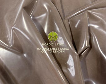 May include: A glossy, taupe-colored sheet of latex with a smooth, reflective surface. The material is draped in folds, showing its flexibility. Text printed on the surface reads: NORDIC LATEX 0.40MM SHEET LATEX CUT TO LENGTH, with a circular logo above.
