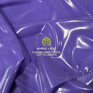 May include: Close-up of a sheet of shiny, purple latex. The text "NORDIC LATEX 0.40MM SHEET LATEX CUT TO LENGTH" is printed on the latex. The latex is folded and has highlights.