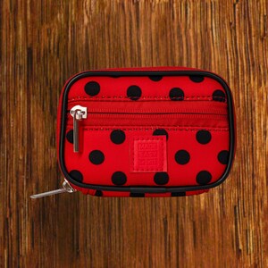 Red Background with Black Polka Dot travel pill organizer case closed, compact zippered medication pouch for daily use, portable storage for vitamins and prescriptions.
