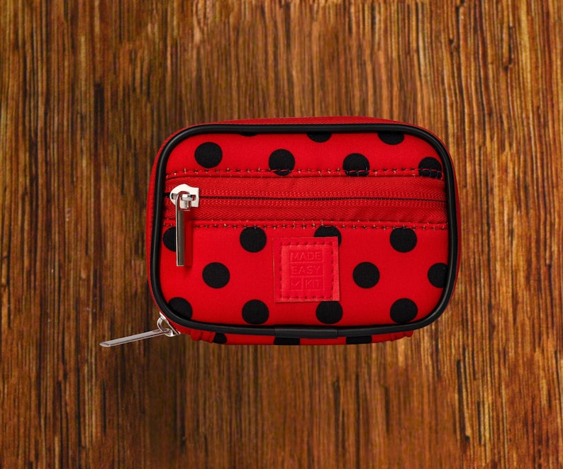 Red Background with Black Polka Dot travel pill organizer case closed, compact zippered medication pouch for daily use, portable storage for vitamins and prescriptions.