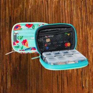 Open floral travel pill organizer case showing interior, weekly pill box and zipper compartments, compact medication storage for on-the-go use