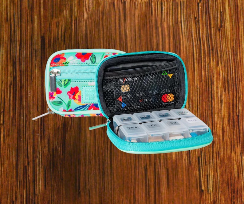 Open floral travel pill organizer case showing interior, weekly pill box and zipper compartments, compact medication storage for on-the-go use