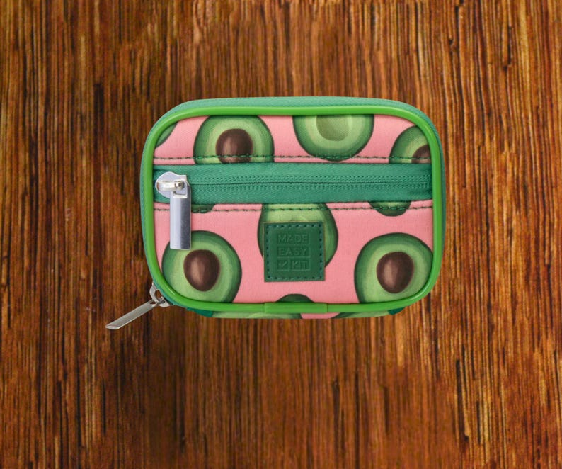 Pink Background with Green Avocado travel pill organizer case closed, compact zippered medication pouch for daily use, portable storage for vitamins and prescriptions.
